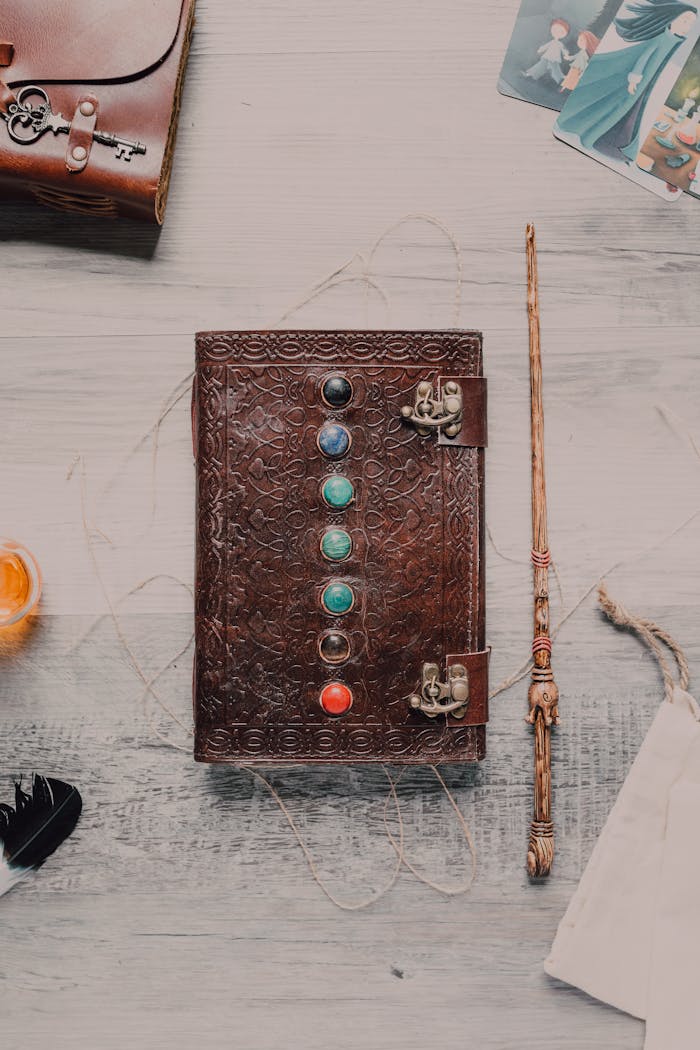 Flat lay of a leather journal with chakra stones, a wand, and mystical elements on a wooden surface.